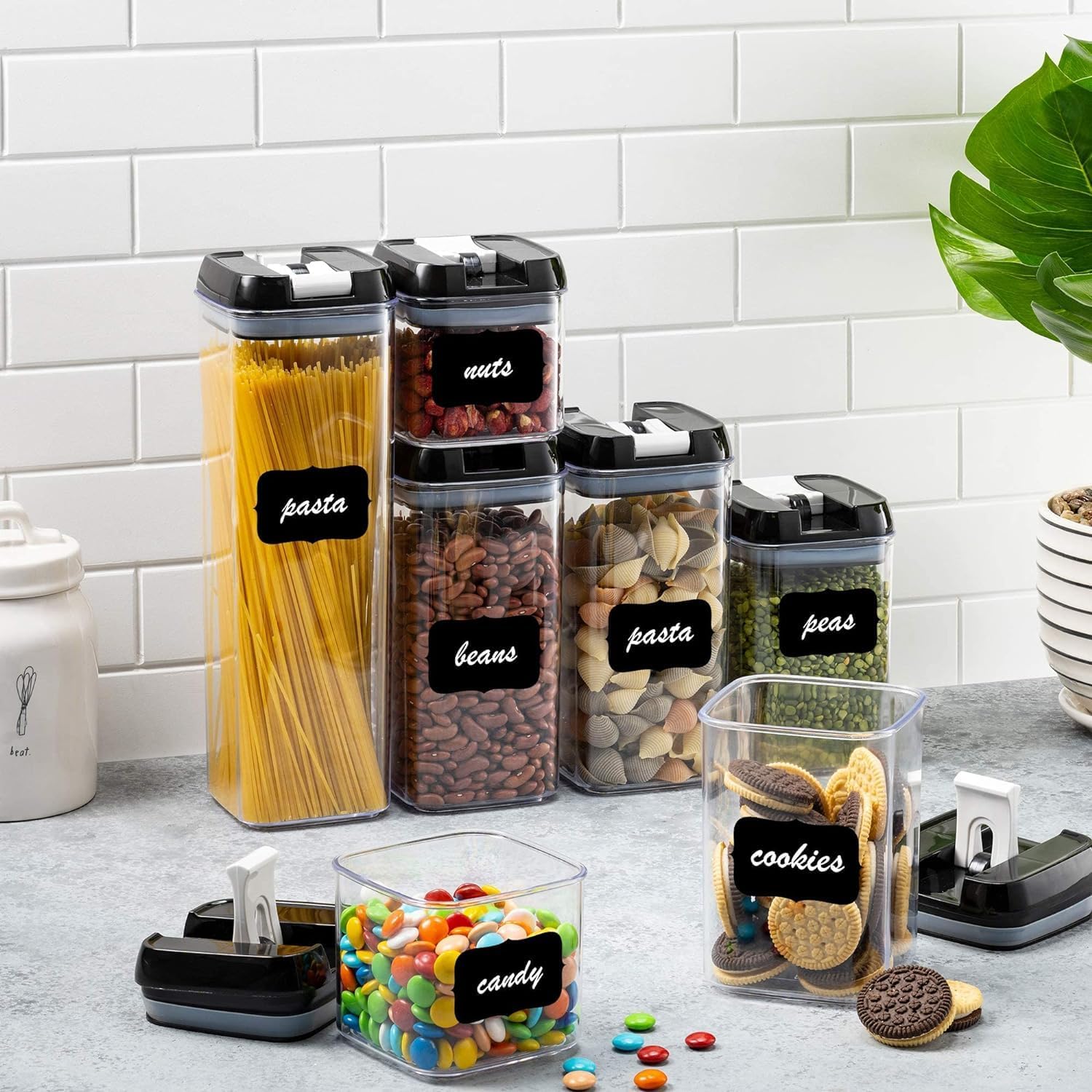 Set of clear storage containers with black lids and labels on a kitchen counter.
