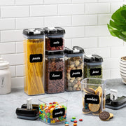 Set of clear storage containers with black lids and labels on a kitchen counter.