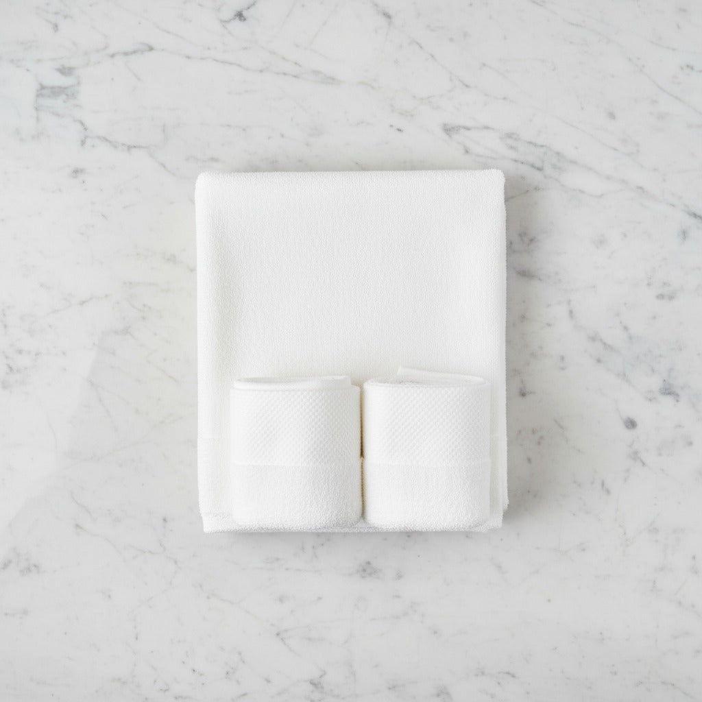 White folded Cotton Bath & Face Towel Set on a marble surface