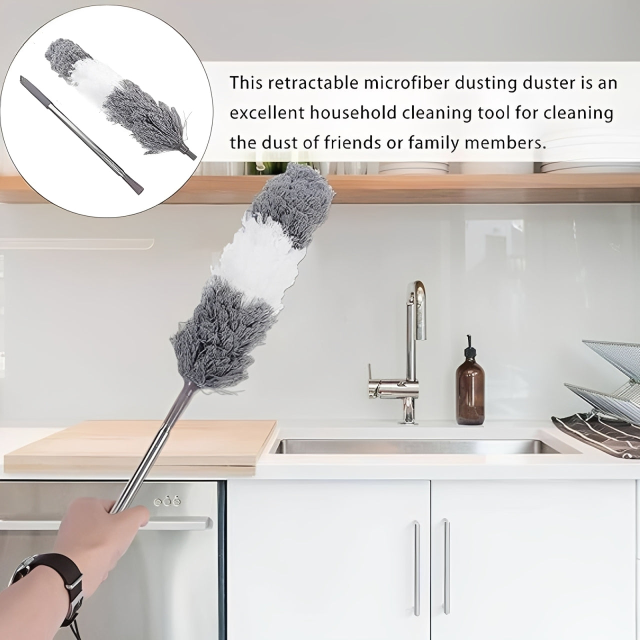 An Extendable Duster for High Ceilings with a long handle and gray-and-white fluffy head is being used in a kitchen. A hand holds the brush near the counter, with a sink, faucet, and cabinet visible.