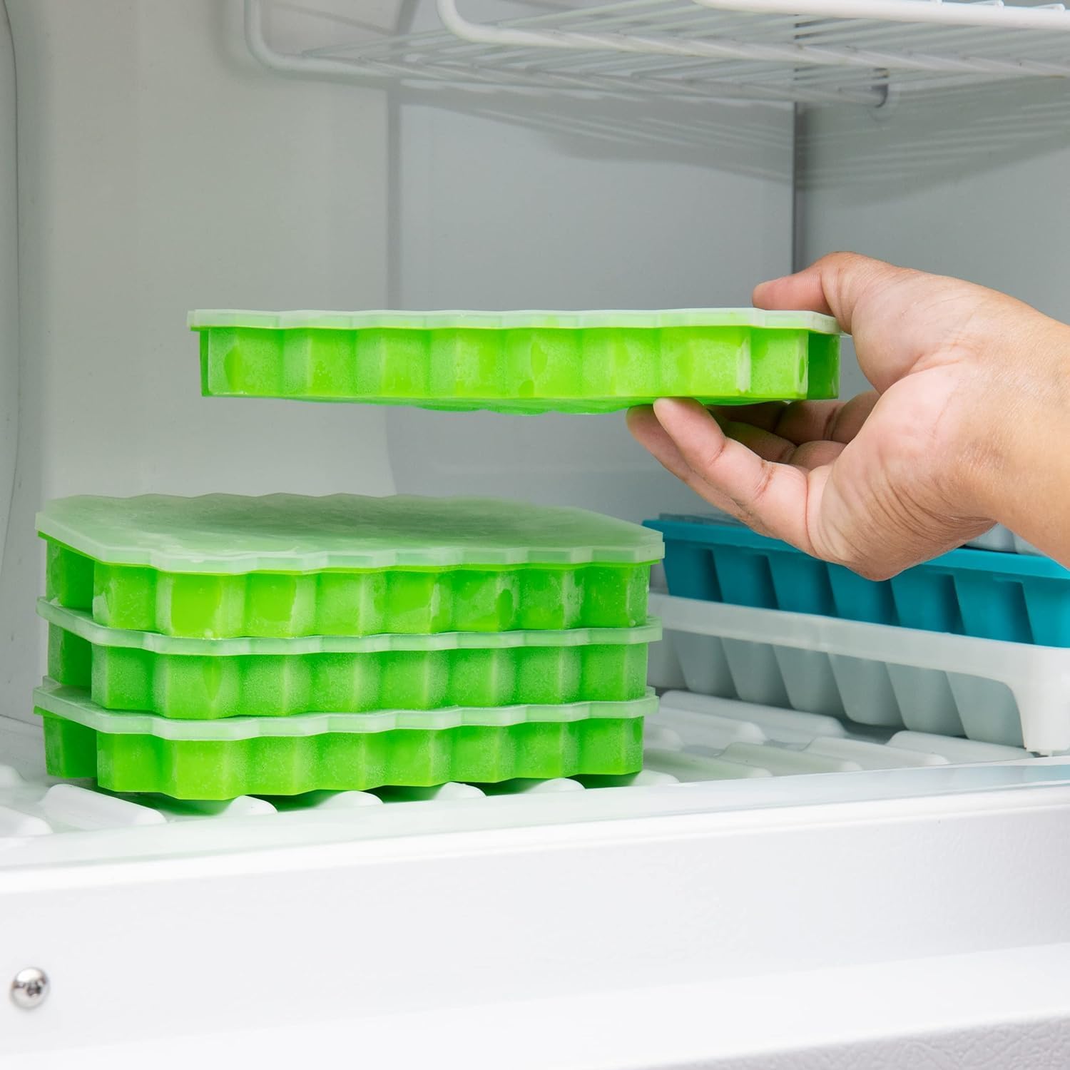 Green Honeycomb Silicone Ice Cube Tray  being held above a freezer with stacked trays inside.