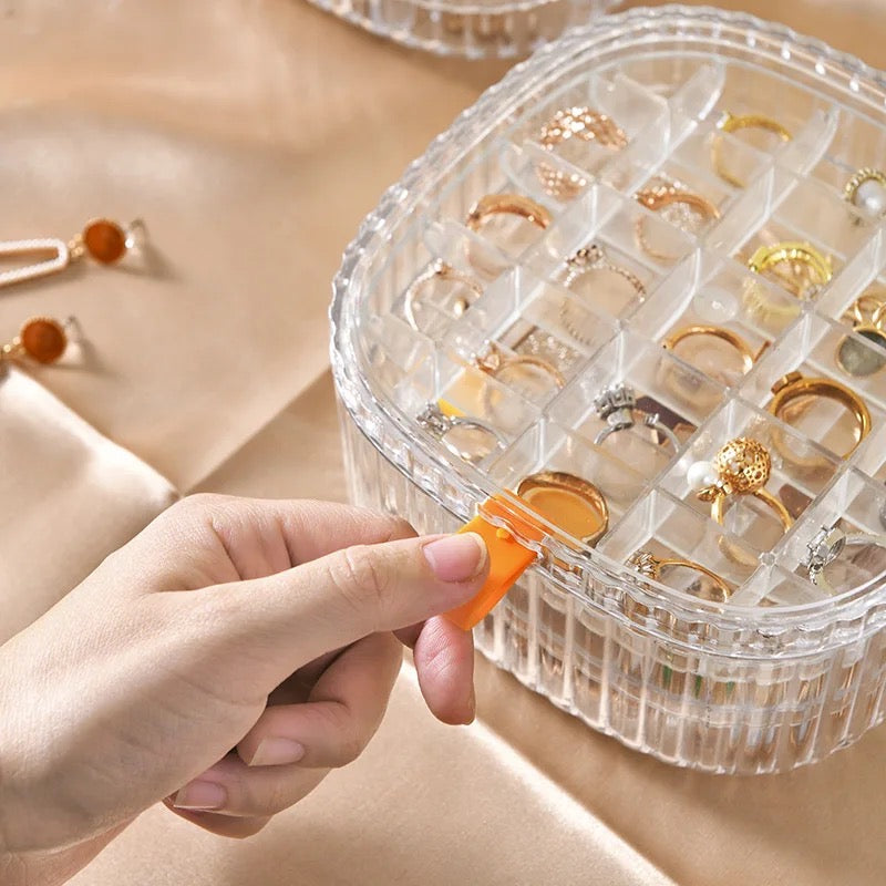 A cosmetic and jewelry storage box with a lid, containing rings and earrings neatly organized inside.