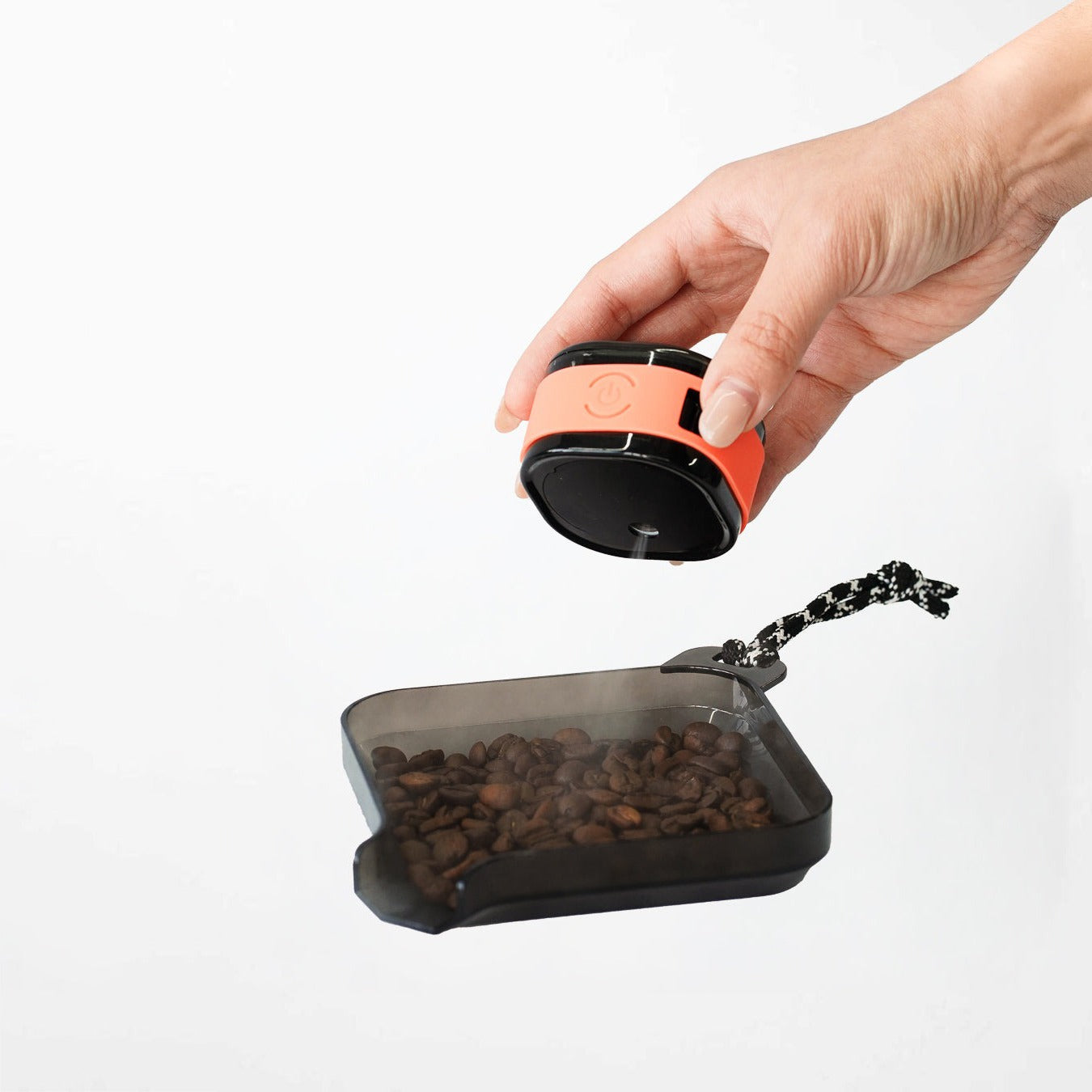 Hand using a Macnoa MacX mistFlow Electric Coffee Atomizer over a tray of coffee beans on a white background