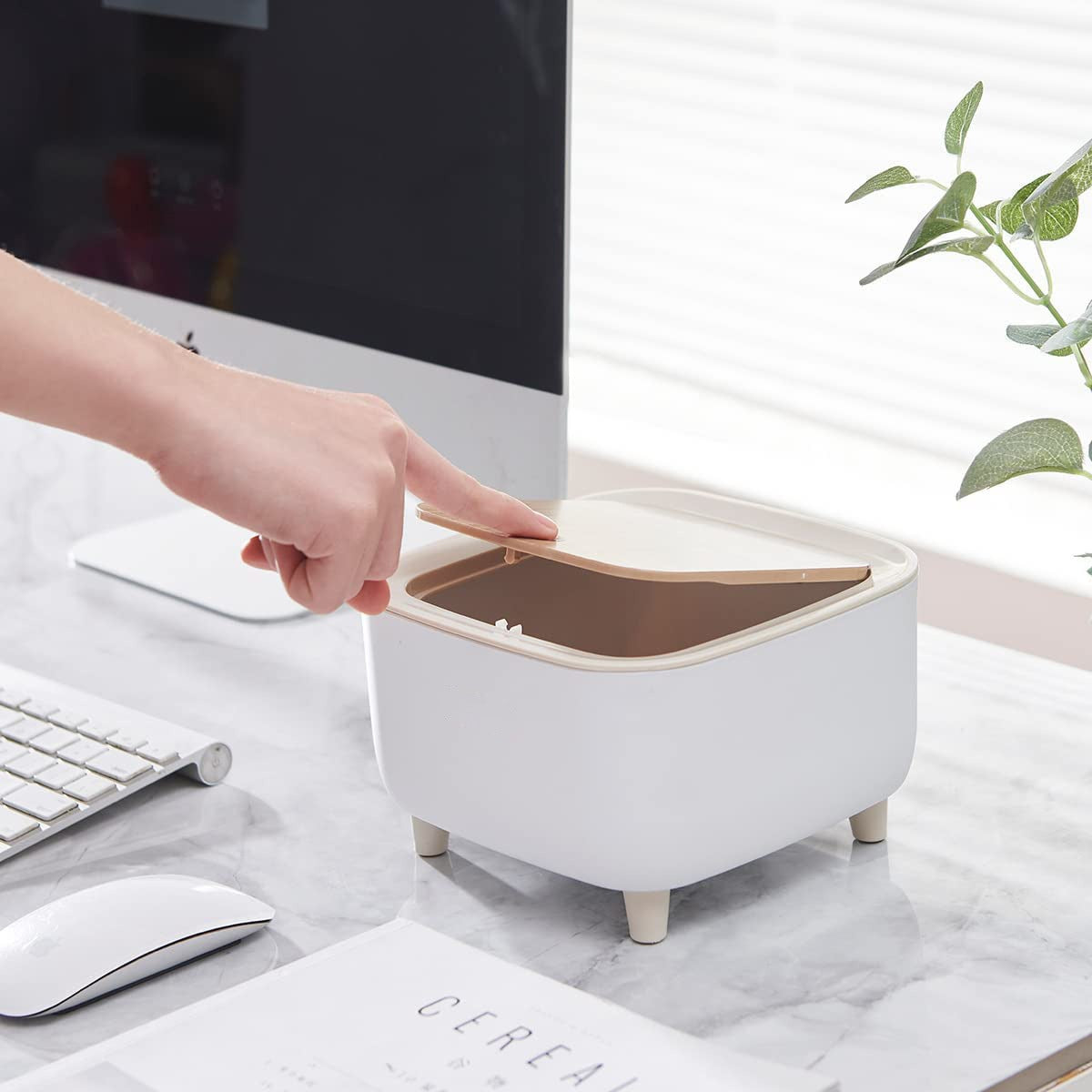 A person is opening the lid of Mini Trash Can kept on a desktop.