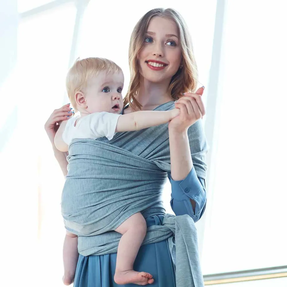 A Women is Holding Her Baby Using Newborn Baby Wrap Carrier Cloth in Grey Color.