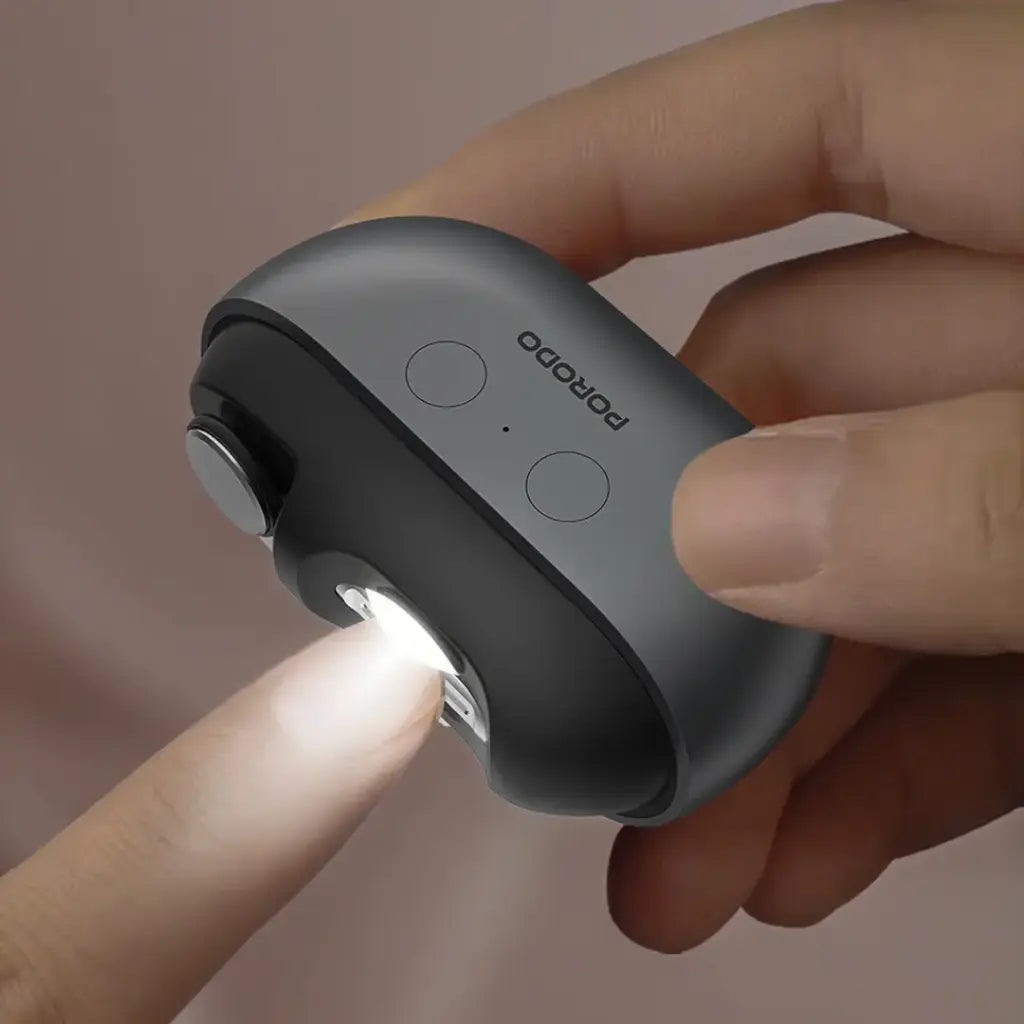 Hand holding a Porodo Multi-Function Electric Nail Clipper on a neutral background