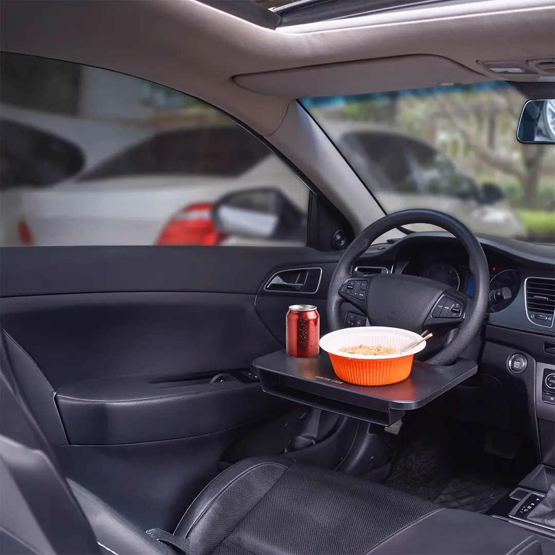 A Green Lion steering wheel tray holding a bowl of food and a drink inside a car, creating a convenient in-car dining setup