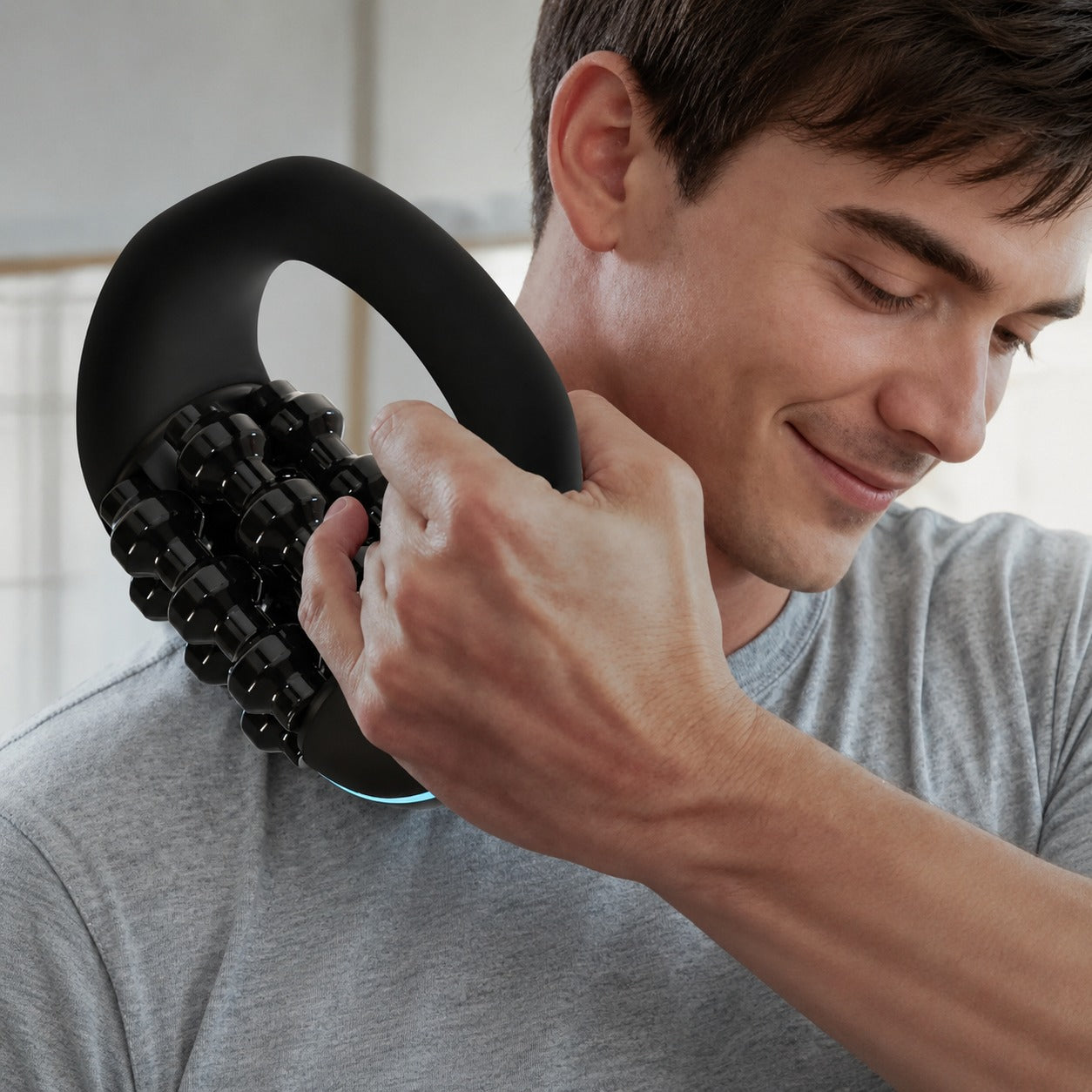 A man using a black Porodo Relieva Roller Massager on his shoulder indoors.