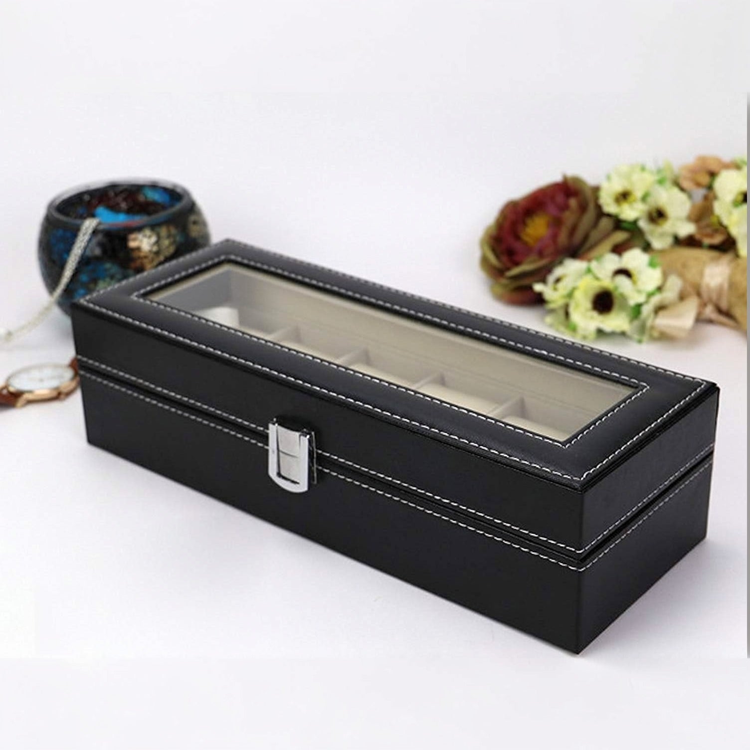 Watch Storage Box with glass top on a white surface with decorative items in the background