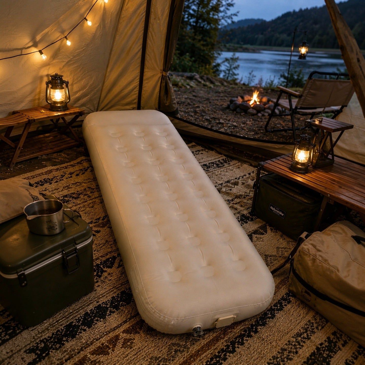 Camping scene with an air mattress, lanterns, and a view of a lake at dusk.