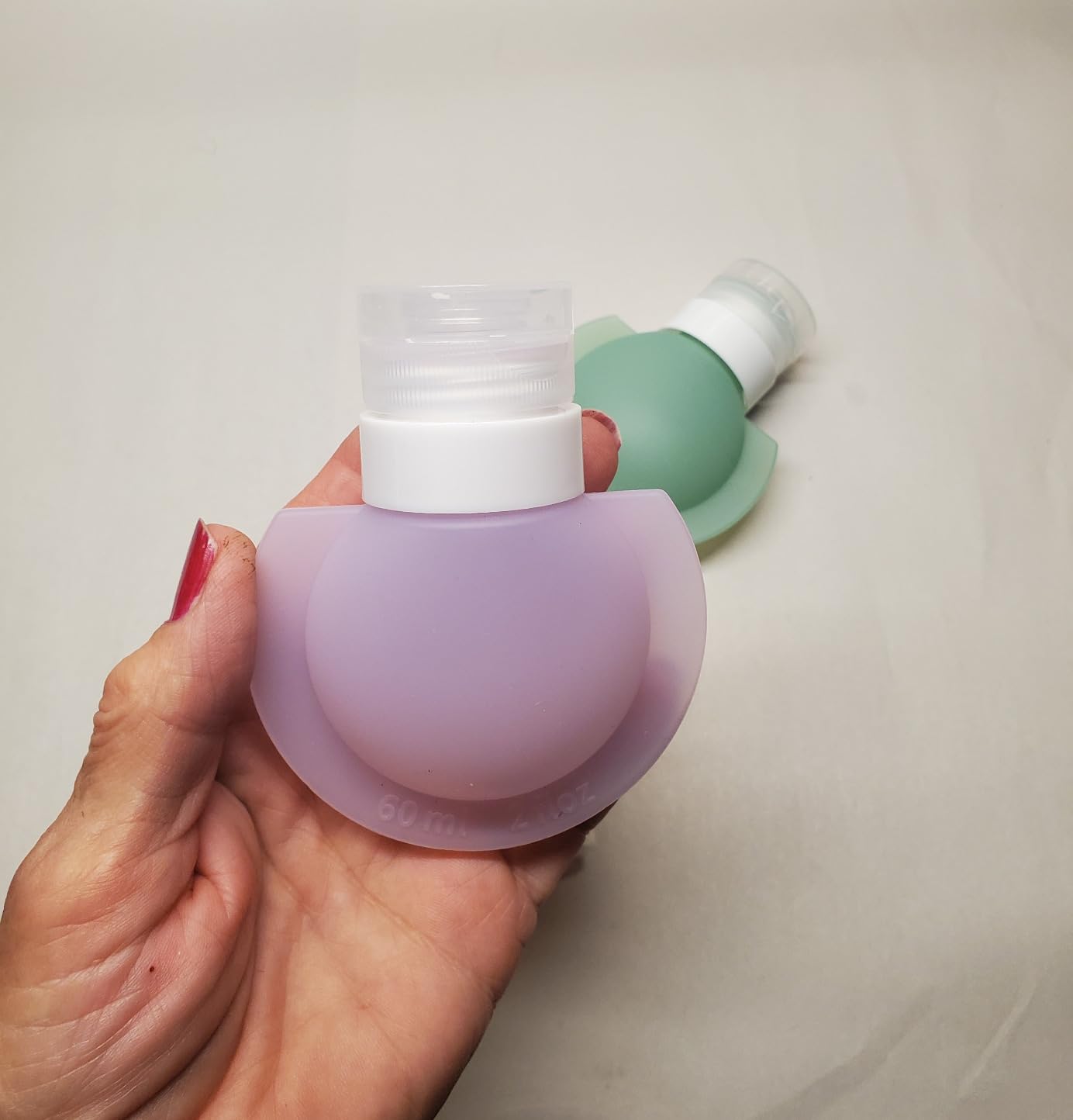 Hand holding a purple Silicone Travel Bottle Set with a white cap against a neutral background