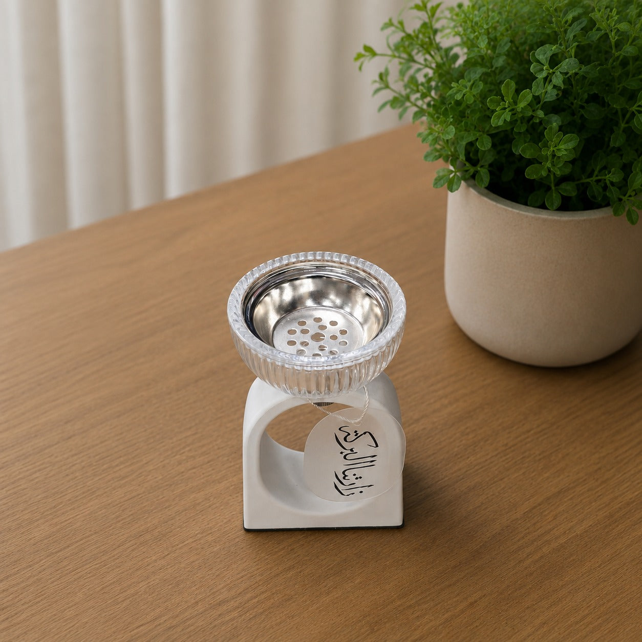 Incense burner  with metal top on a wooden surface next to a potted plant.